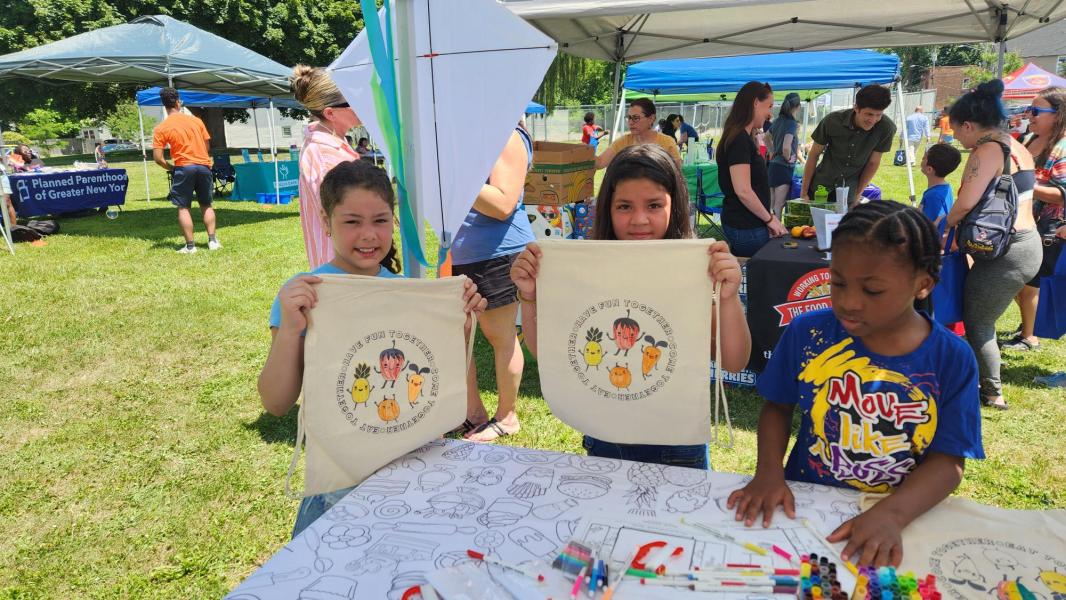 Three kids coloring Summer Meals Bags two are holding them up