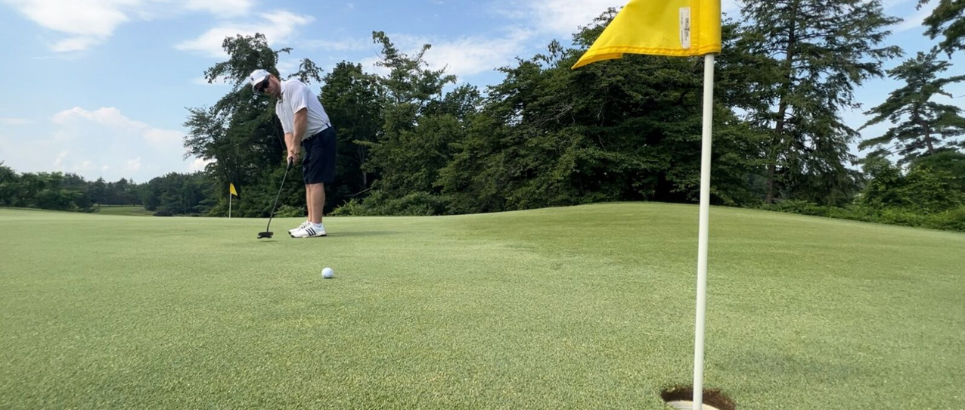 Golfer putting into a hole with a yellow flag inside