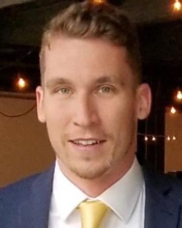 Ethan in blue suit yellow tie smiling with string of light in background