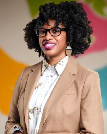 Simone in glasses smiling in brown blazer