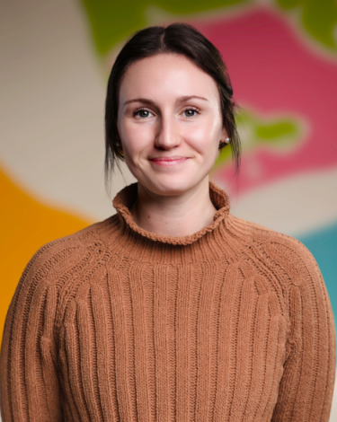 Allison in brown turtleneck smiling against colorful wall