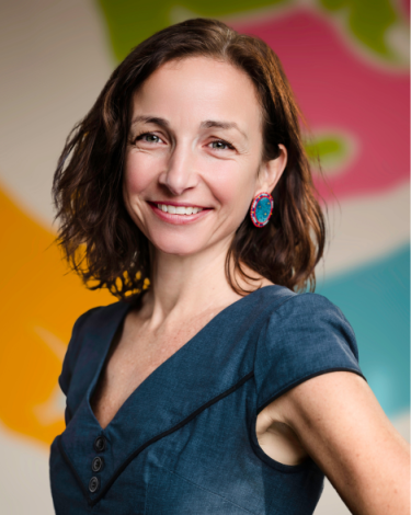 Claire in blue dress smiling against colorful wall