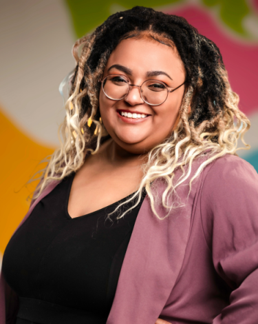 Faith smiling in pink blazer with black shirt against colorful wall