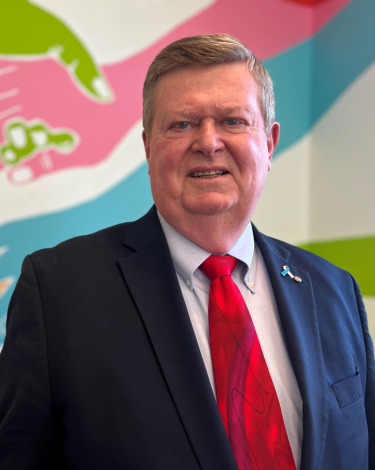 Fred in black suit red tie smiling against colorful wall
