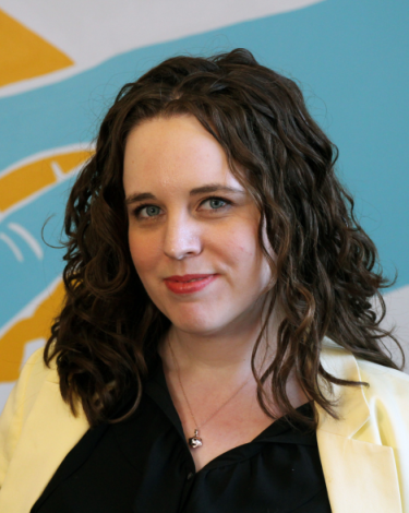 Heather-Liz smiling in black shirt with cream blazer against colorful wall