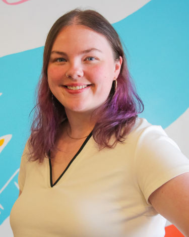 Keady in cream shirt smiling against colorful wall