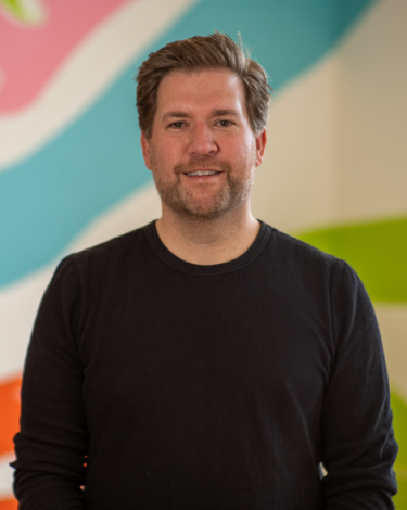 peter in black shirt smiling against colorful wall
