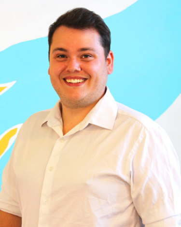 William in white shirt smiling against colorful wall