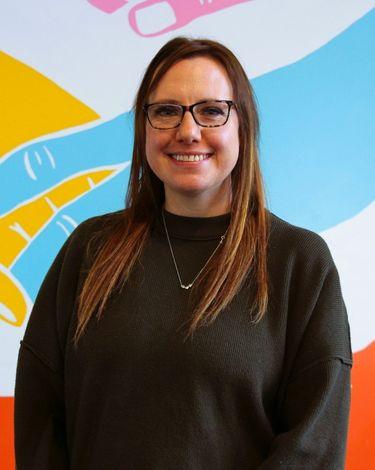 Alicia smiling in green sweater against colorful wall