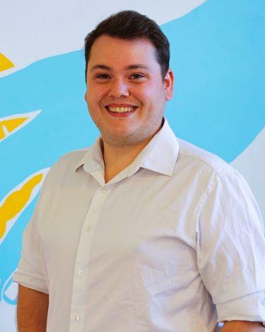 William in white button-up smiling against colorful wall