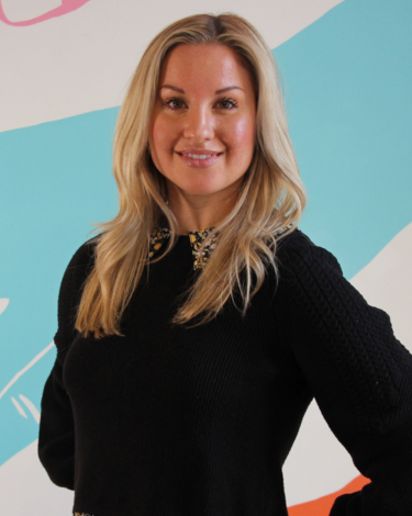 Annie smiling in black shirt against colorful hand wall