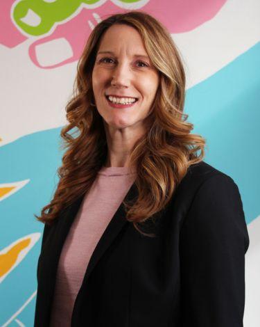 Melissa smiling with black blazer and pink shirt against colorful hand wall