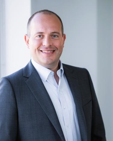 Ryan Case smiling in gray blazer with white shirt